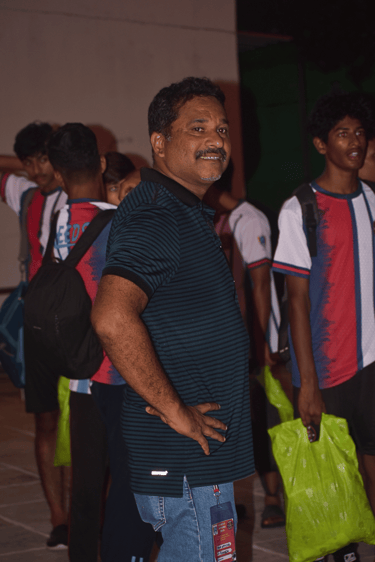 Smiling man in a blue striped polo shirt standing with a group of young athletes in jerseys.