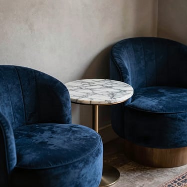 A refined, intimate corner of a lounge with deep blue velvet chairs and a small marble table, South American / Brazilian interior design.