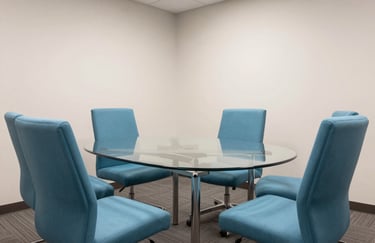 A modern, bright North American / US corporate meeting room with sea blue chairs and a glass table.