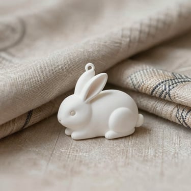 A minimal white rabbit charm symbolizing peace, resting on a pile of traditional Kyoto woven fabrics in soft neutral tones.
