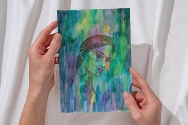 Hände halten ein farbenfrohes Aquarellporträt einer Frau mit blauen und grünen abstrakten Pinselstri