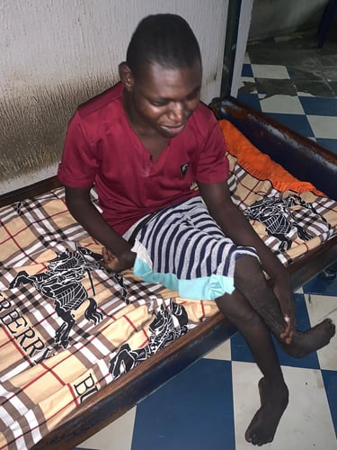A young man with physical disabilities sitting on a patterned bed in a room with blue and white tiles.