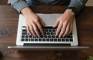 Top-down view of professional hands working on a laptop at a dark wooden desk, focused lighting, Southern European office context.