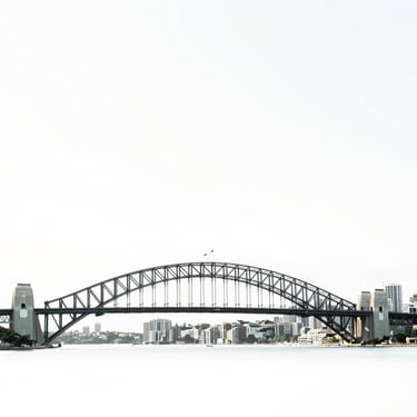 Minimalist architectural photography of Sydney harbor bridge and skyline in bright natural daylight, clean white and subtle green tones, high-end editorial