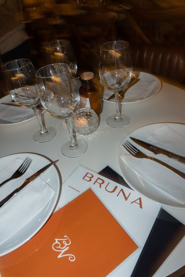 Elegante mesa preparada en Bruna, con copas de vino, platos blancos y cubiertos.