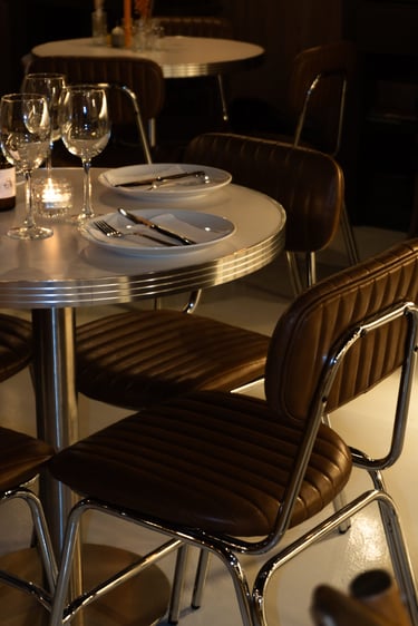 Elegante mesa de bistró preparada con sillas de cuero, copas de vino y cubertería de plata.