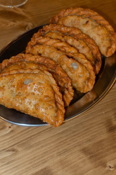 Empanadas doradas y crujientes servidas en una bandeja de plata sobre una mesa de madera.