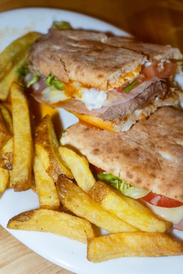 Sándwich gourmet de carne con huevo y queso, acompañado de crujientes patatas fritas doradas.