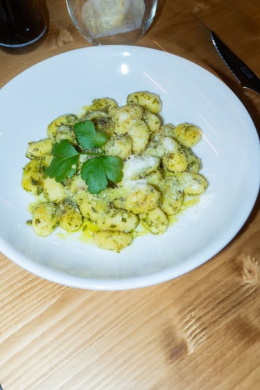 Ñoquis de patata fresca con pesto de albahaca y queso parmesano, servidos en un plato blanco.