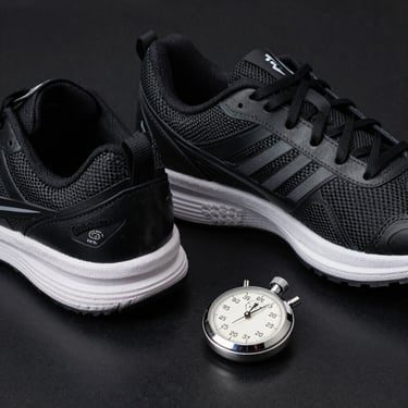 A pair of professional athletic shoes and a stopwatch on a polished black surface, sharp focus, sophisticated Carbon Black and Smoke White color palette, Global / Spanish-speaking.