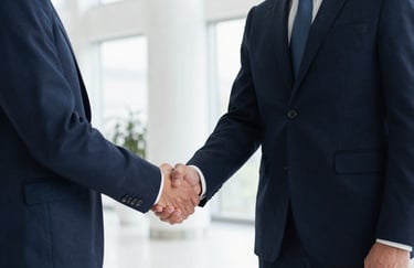 A sharp, medium-shot photograph of two professionals in dark navy blue suits shaking hands in a bright, modern lobby, emphasizing trust.