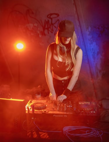 Female DJ in a black cap mixing music on a Pioneer DJ controller with red and blue stage lighting.