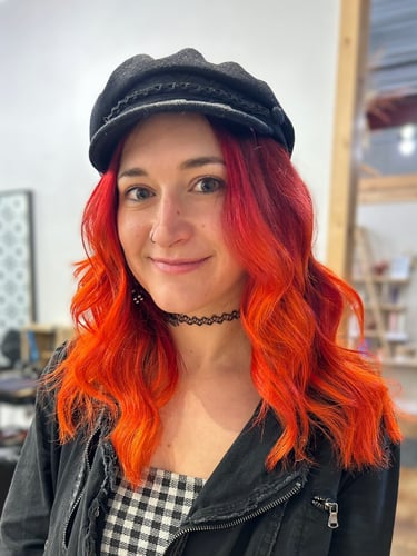 Kristen in a newsboy hat and leather jacket with vibrant red-orange hair..