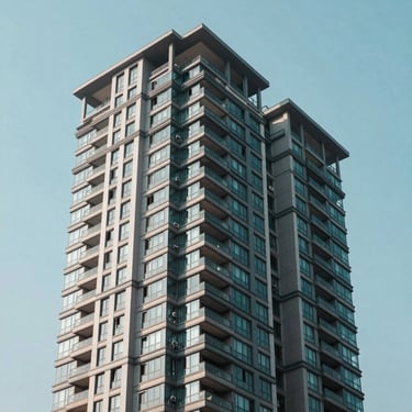 Modern South Asian residential high-rise building with glass balconies against a clear light blue sky.