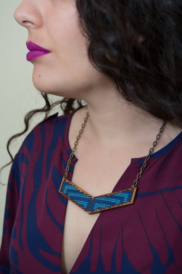 Una mujer luce un collar azul bordado a mano con motivos geométricos, sujeto a un colgante de madera