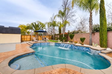 Luxury backyard swimming pool with waterfalls, palm trees, and a sun deck for outdoor relaxation.