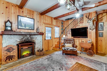 Cozy lodge-style living room featuring a stone fireplace, wood panel walls, and a leather armchair.