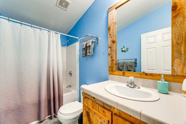 A bright blue bathroom with rustic wooden vanity and white tiled shower-tub combo.