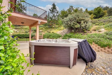 Outdoor luxury hot tub on a concrete patio overlooking a lush green hillside landscape.