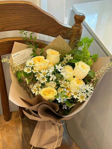 ramo de rosas amarillas con follaje verde margaritas color blanco envueltas en papel cafe 