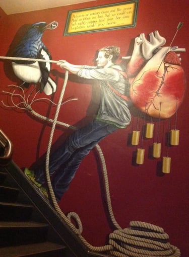 Surreal mural on a red wall showing a man pulling a rope attached to a bird and an anatomical heart.