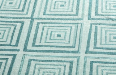 Close-up photography of a textile pattern design featuring complex geometric shapes in pale mint and muted teal on fine fabric.