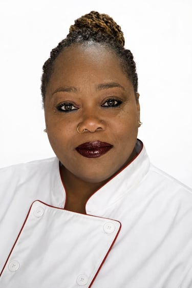 Professional portrait of a female chef in a white culinary coat with red piping.