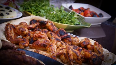 Grilled chicken wings served on flatbread with fresh herbs and roasted peppers for a BBQ feast.