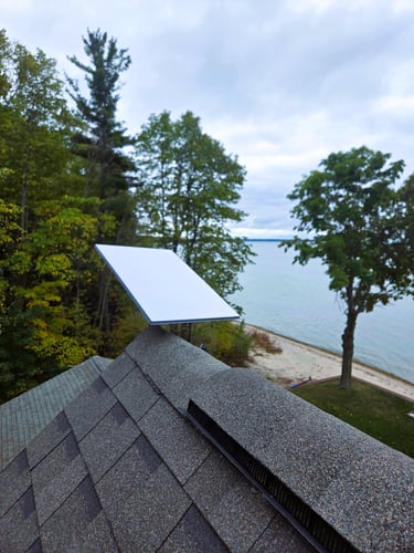 Rooftop Starlink dish overlooking lakefront property with trees, beach, and water.