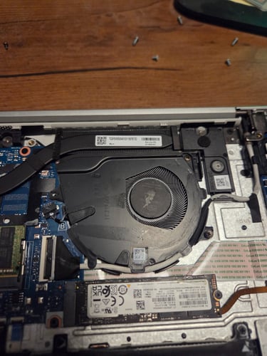 Open laptop showing internal components including fan, SSD, cables, and motherboard.