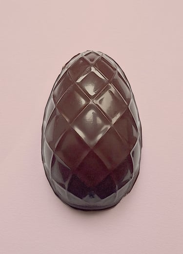 A dark chocolate Easter egg with a quilted diamond pattern on a soft pink background.