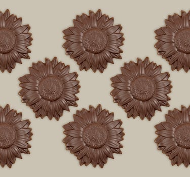 A pattern of gourmet dark chocolate sunflower shaped candies on a neutral background.