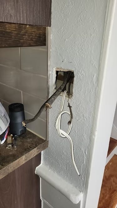 Exposed electrical wiring protruding from a hole in a gray wall during home renovation.