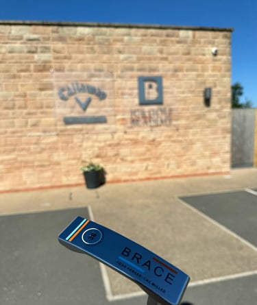 Brace forged golf putter in front of brick wall