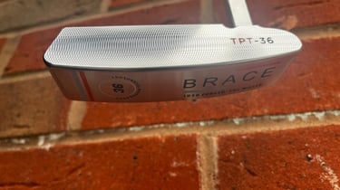 Brace forged golf putter in front of brick wall