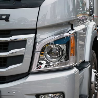 Close-up detail of a modern truck's headlight and chrome grill, reflecting a professional Brazilian cargo terminal environment, clean and high-tech feel.