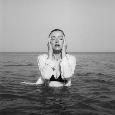 Portrait en noir et blanc à la pellicule argentique d'une femme qui porte une chemise blanche dans la mer