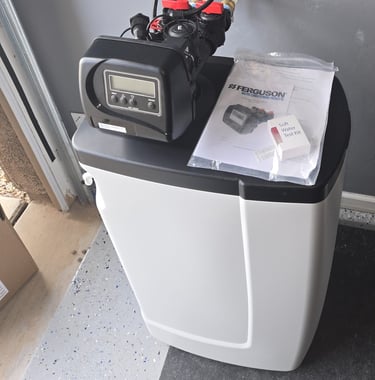 A Ferguson water softener system with digital control head and soft water test kit in a garage.