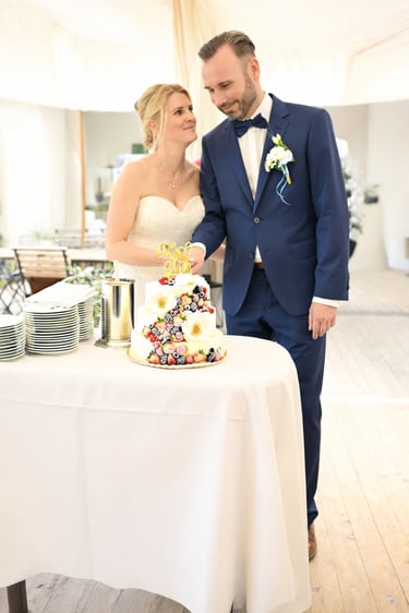 Brautpaar beim Anschneiden der Hochzeitstorte in heller Hochzeitslocation