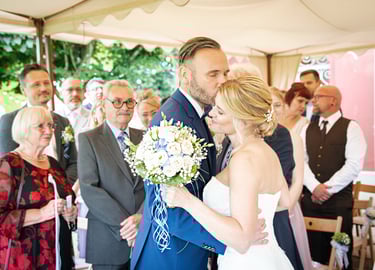 Brautpaar bei der Trauung, emotionaler Moment mit Gästen im Hintergrund