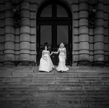 Emotionales Hochzeitsfoto in Schwarz-Weiß Zwei Bräute Hand in Hand vor dem prachtvollen Portal eines Prager Palastes.