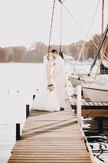 Brautpaar bei einem Hochzeitsshooting auf einem Steg am See mit Segelbooten im Hintergrund