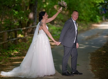 Brautpaar geht Hand in Hand einen Waldweg entlang, die Braut hält den Brautstrauß erhoben.
