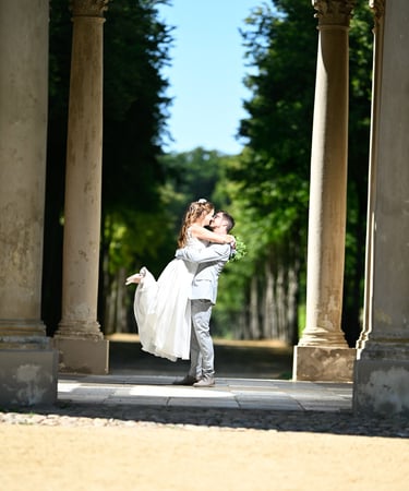 Hochzeitsfoto: Bräutigam hebt Braut zwischen Steinsäulen hoch.