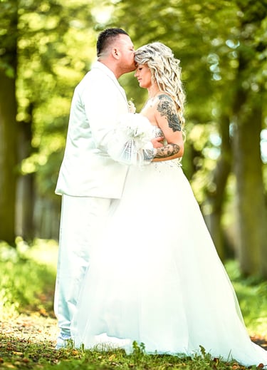 Bräutigam küsst die Stirn der Braut im Wald, emotionale Hochzeitsfotografie mit natürlichem Licht
