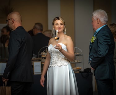Braut beim Sektempfang hält ein Glas Sekt, Hochzeitsgäste im Hintergrund