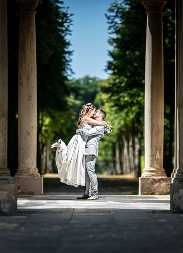 Bräutigam hebt die Braut im Säulengang, romantische Hochzeitsfotografie im Grünen