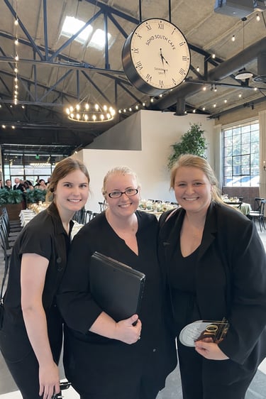 Event staff smiling inside Soho South Cafe in Savannah, featuring industrial decor and string lights.