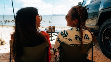 Two women sitting and chatting beside their Toyota FJ Cruiser on the beach in Okinawa. | Evertrail Okinawa