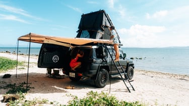 The Toyota FJ Cruiser with its roof tent fully extended. One person climbs the ladder, the other organizes inside.